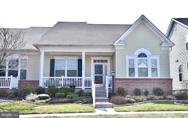 view of front facade featuring covered porch, brick siding, and roof with shingles