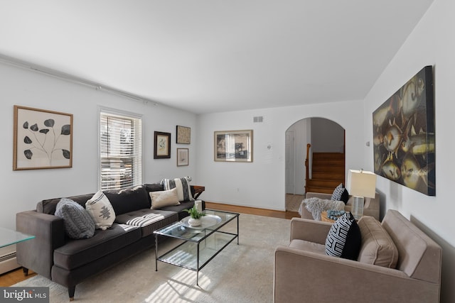 living room with light wood-style flooring, arched walkways, visible vents, and stairway