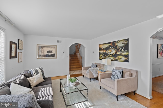 living area with arched walkways, visible vents, stairway, light wood-type flooring, and baseboards