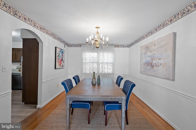 dining room with a chandelier, arched walkways, wood finished floors, and baseboards