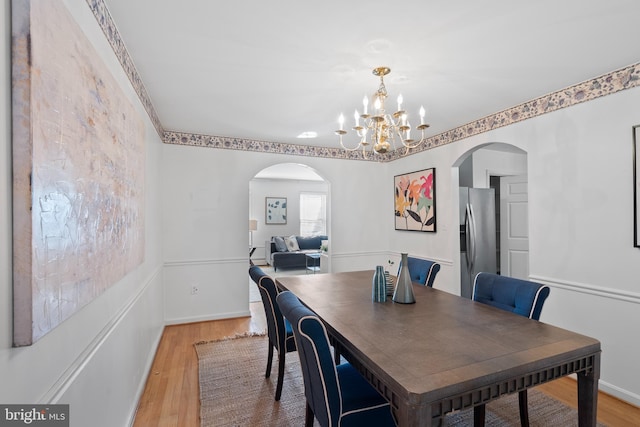 dining space featuring arched walkways, light wood-type flooring, baseboards, and a notable chandelier