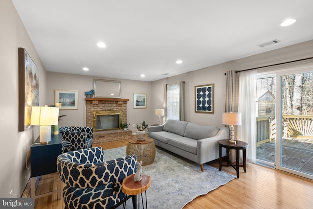 living area with a brick fireplace, wood finished floors, visible vents, and recessed lighting