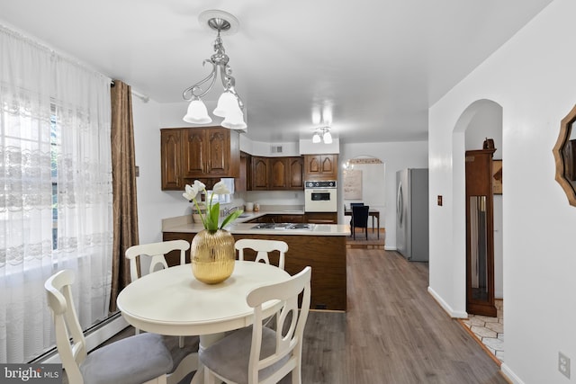 dining space featuring light wood finished floors, a baseboard radiator, arched walkways, and baseboards