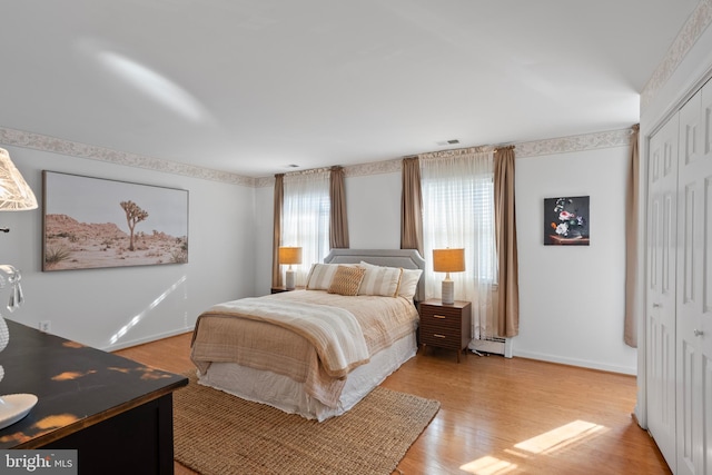 bedroom featuring visible vents, baseboards, light wood-style flooring, baseboard heating, and a closet