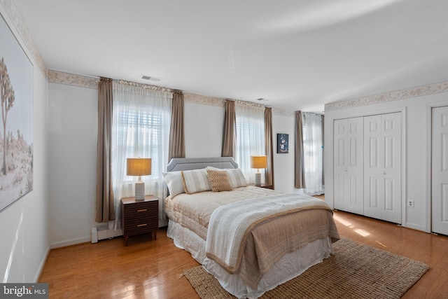 bedroom featuring baseboards, visible vents, wood finished floors, baseboard heating, and two closets