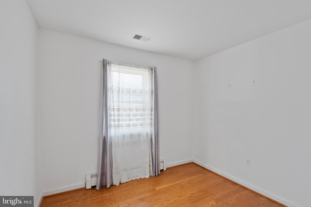 empty room with light wood-style floors, a baseboard radiator, visible vents, and baseboards