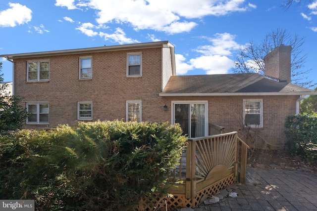 back of house with a deck, brick siding, a chimney, and a patio area