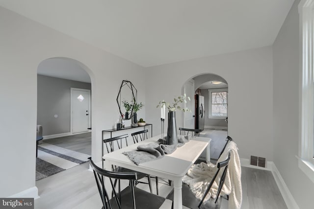 dining area with visible vents, arched walkways, light wood finished floors, and baseboards