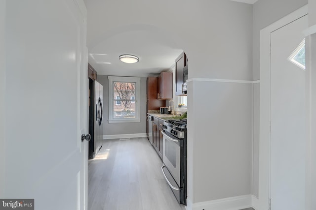 kitchen with baseboards, a sink, light countertops, appliances with stainless steel finishes, and light wood-type flooring