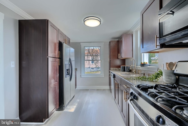 kitchen with baseboards, light stone countertops, light wood-type flooring, stainless steel appliances, and a sink