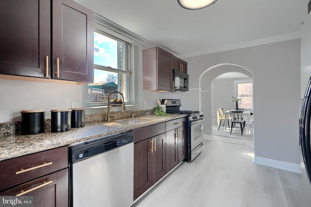 kitchen featuring ornamental molding, light stone counters, arched walkways, stainless steel appliances, and a sink