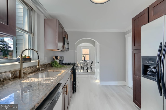 kitchen with ornamental molding, a sink, dark stone countertops, arched walkways, and appliances with stainless steel finishes