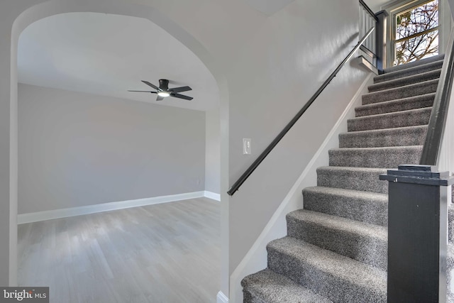 stairway featuring ceiling fan, baseboards, arched walkways, and wood finished floors