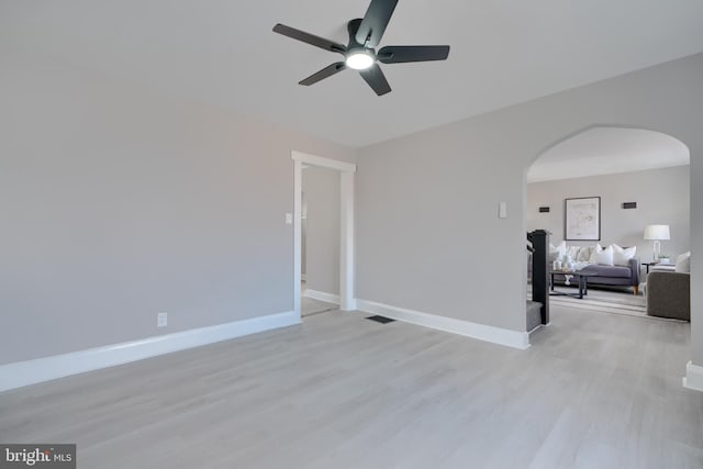 empty room featuring light wood-type flooring, visible vents, arched walkways, baseboards, and ceiling fan