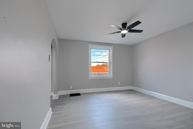 unfurnished room featuring visible vents, a ceiling fan, arched walkways, light wood-style floors, and baseboards