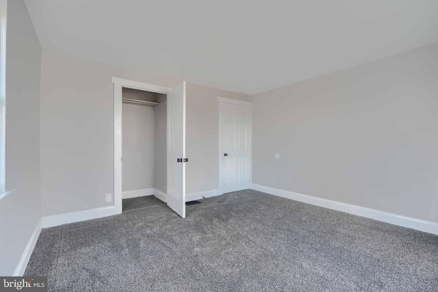 unfurnished bedroom with a closet, dark carpet, and baseboards