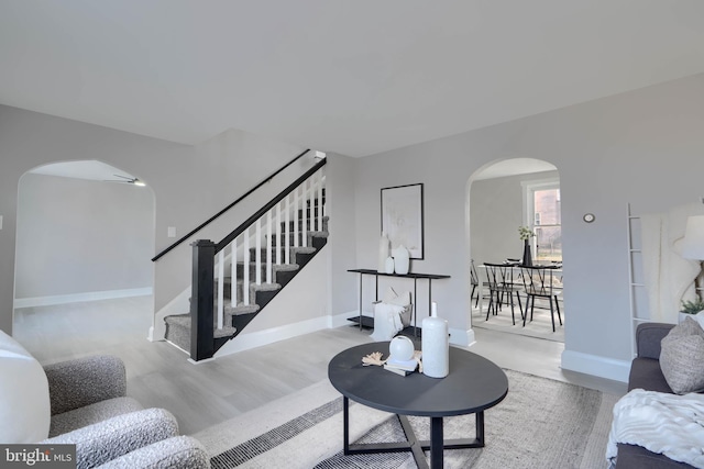 living area featuring stairs, wood finished floors, baseboards, and arched walkways