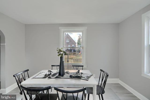 dining area with light wood-style flooring, baseboards, and arched walkways