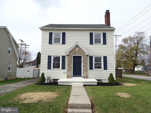 colonial house featuring stone siding, a chimney, fence, and a front lawn