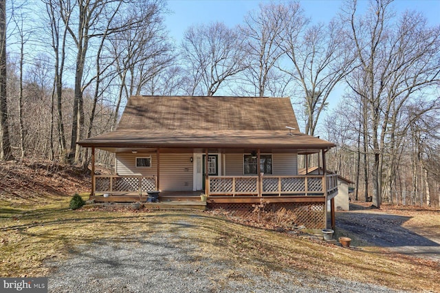 view of front of home featuring a porch, roof with shingles, and gravel driveway