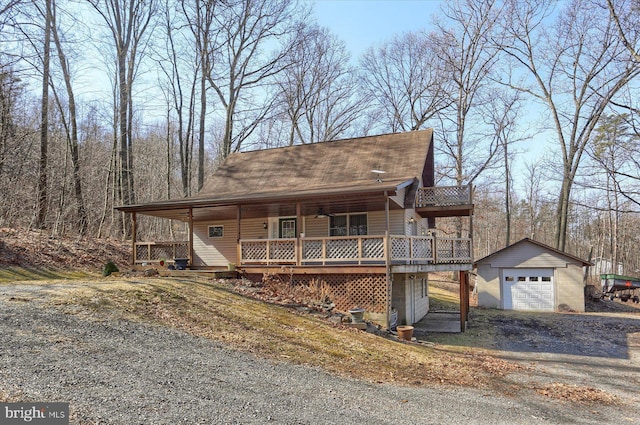 view of front of property with a shingled roof, a detached garage, aphalt driveway, a porch, and an outbuilding