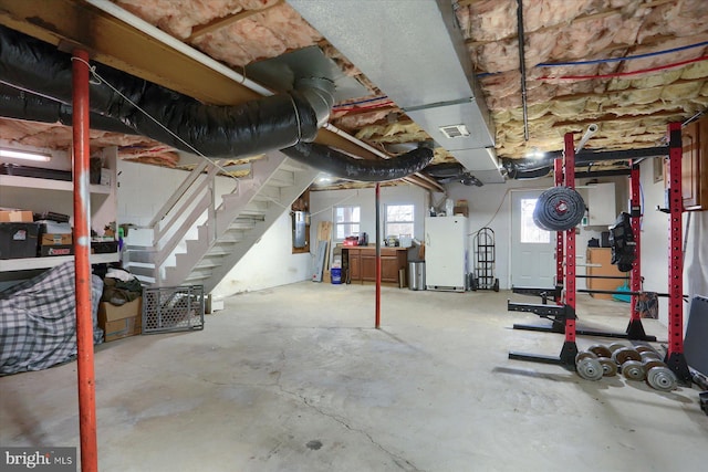 basement with electric panel, visible vents, and freestanding refrigerator