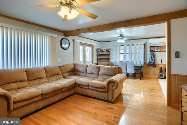 living room featuring a wainscoted wall, beam ceiling, light wood-style flooring, a wall mounted AC, and crown molding