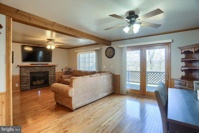 living area featuring light wood-type flooring, plenty of natural light, beam ceiling, and wainscoting