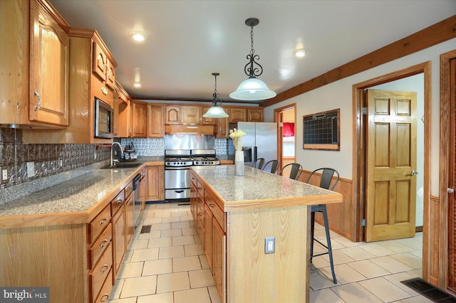 kitchen with a center island, a breakfast bar, wainscoting, appliances with stainless steel finishes, and a sink