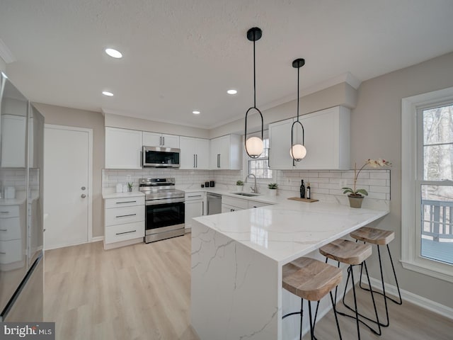 kitchen with light stone countertops, a breakfast bar, a peninsula, stainless steel appliances, and a sink