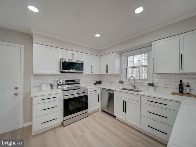 kitchen with a sink, backsplash, stainless steel appliances, light wood-style floors, and white cabinets