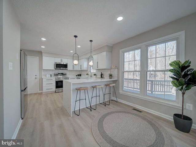 kitchen with a breakfast bar area, visible vents, a peninsula, stainless steel appliances, and tasteful backsplash