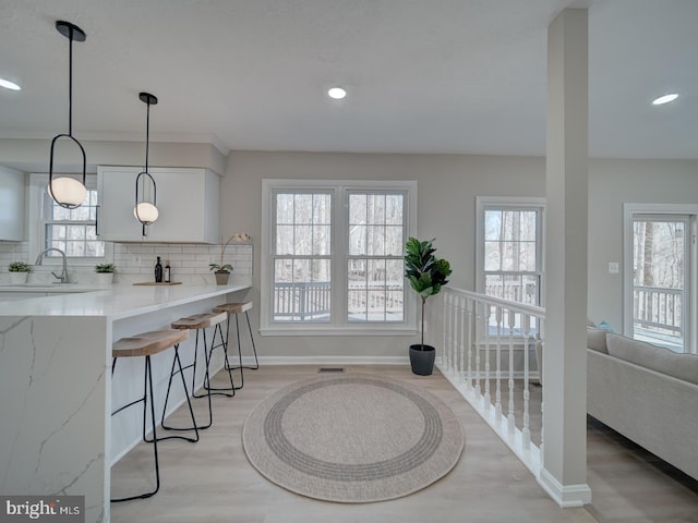 kitchen with a breakfast bar, light stone counters, decorative backsplash, light wood-style floors, and a sink