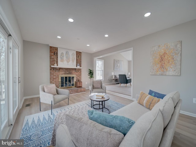 living room with recessed lighting, visible vents, a brick fireplace, and wood finished floors