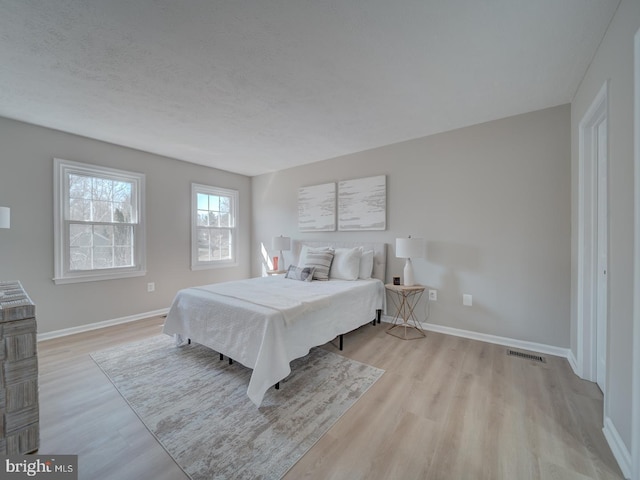 bedroom with visible vents, a textured ceiling, baseboards, and wood finished floors