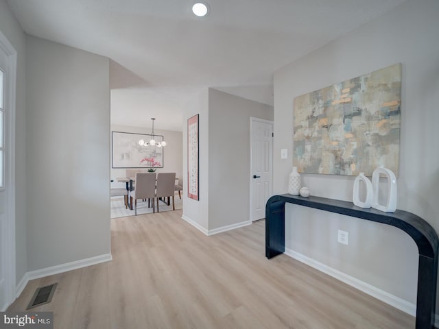 hallway featuring visible vents, baseboards, a notable chandelier, and wood finished floors