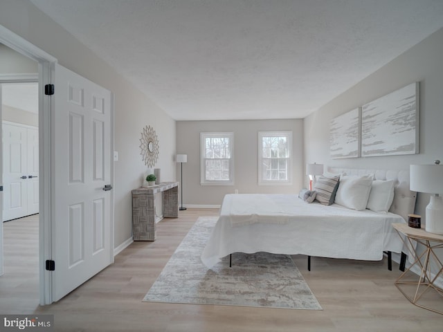 bedroom featuring a textured ceiling, baseboards, and light wood-style floors