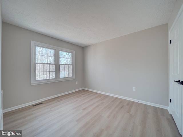 spare room featuring visible vents, baseboards, a textured ceiling, and light wood finished floors