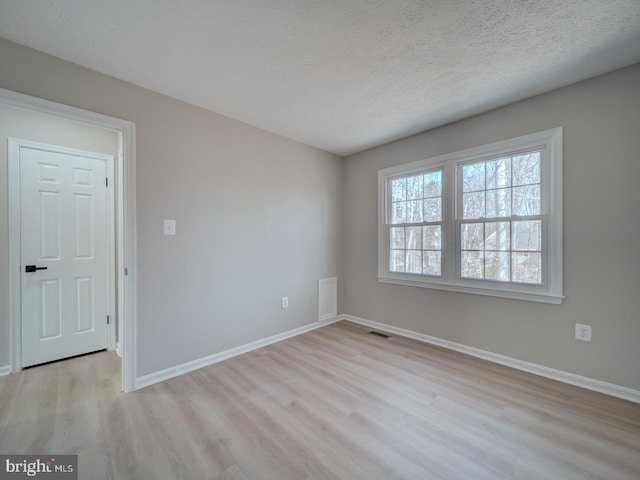 spare room featuring light wood-style flooring, baseboards, visible vents, and a textured ceiling