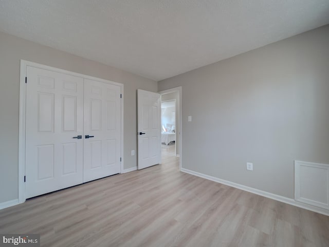 unfurnished bedroom featuring a closet, a textured ceiling, baseboards, and light wood-style floors