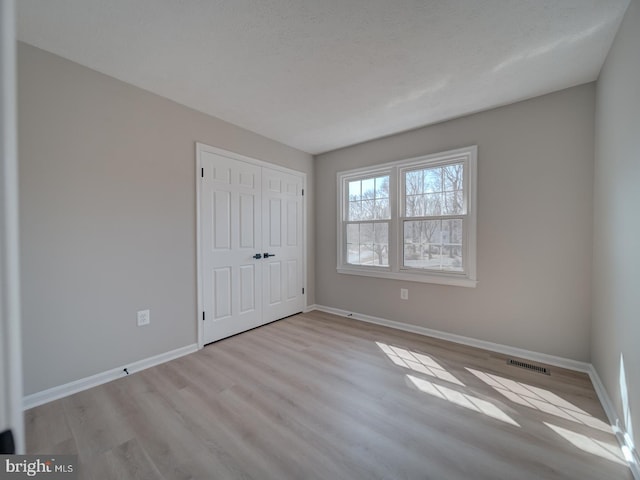 unfurnished bedroom featuring wood finished floors, baseboards, visible vents, and a closet