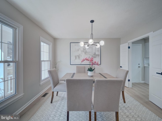 dining area featuring an inviting chandelier, baseboards, visible vents, and light wood finished floors