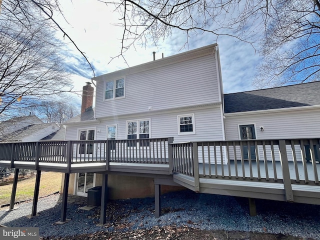 rear view of property featuring a deck, central AC unit, roof with shingles, and a chimney