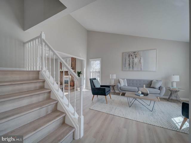 living room featuring baseboards, high vaulted ceiling, wood finished floors, and stairs