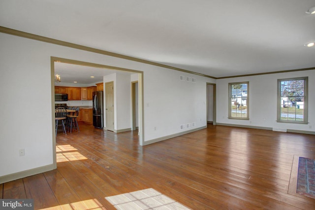 unfurnished living room featuring hardwood / wood-style floors, crown molding, visible vents, and baseboards