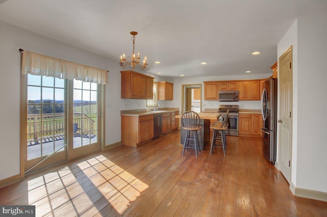 kitchen with light wood-style flooring, a sink, a center island, appliances with stainless steel finishes, and light countertops