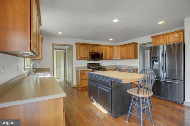 kitchen with recessed lighting, a sink, dark wood-type flooring, appliances with stainless steel finishes, and a center island