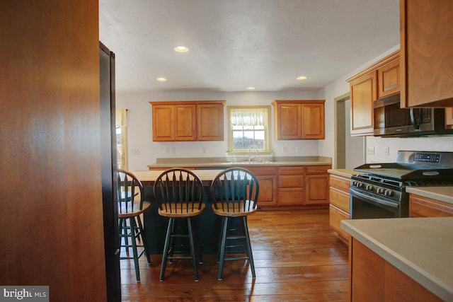 kitchen with a sink, a kitchen breakfast bar, appliances with stainless steel finishes, light countertops, and dark wood-style flooring