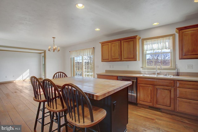 kitchen with a sink, dishwasher, light wood-style flooring, and brown cabinetry