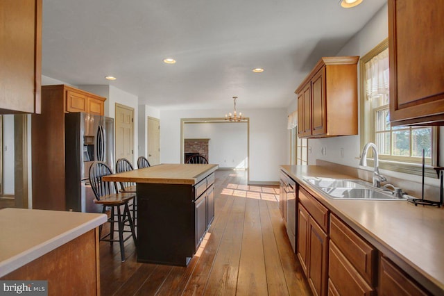 kitchen featuring dark wood-style floors, a sink, appliances with stainless steel finishes, a kitchen bar, and a brick fireplace